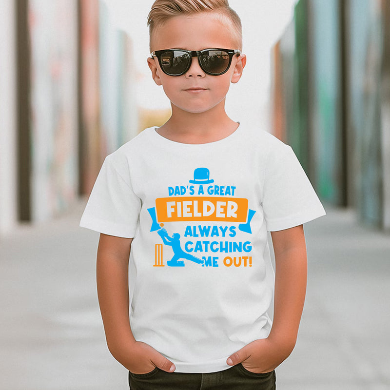 A little boy wearing a white t-shirt with Funny Kids Cricket T-Shirt – “Dad Is a Great Fielder, Always Catching Me Out” on the front. A funny cricket t-shirt Premium Fabric, Multiple Junior Sizes, Perfect for Boys and Girls
