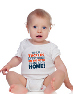 Baby wearing a white onesie with colorful text on a white background, with a slogan on the front saying 'My Mum Tackles Everything on the Pitch and at Home!'