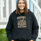 Woman wearing a black hoodie with rugby text design outdoors, with slogan on the front 'Rugby Is a Hooligan’s Game Played by Gentleman, and Football Is a Gentleman’s Game Played by Hooligans
