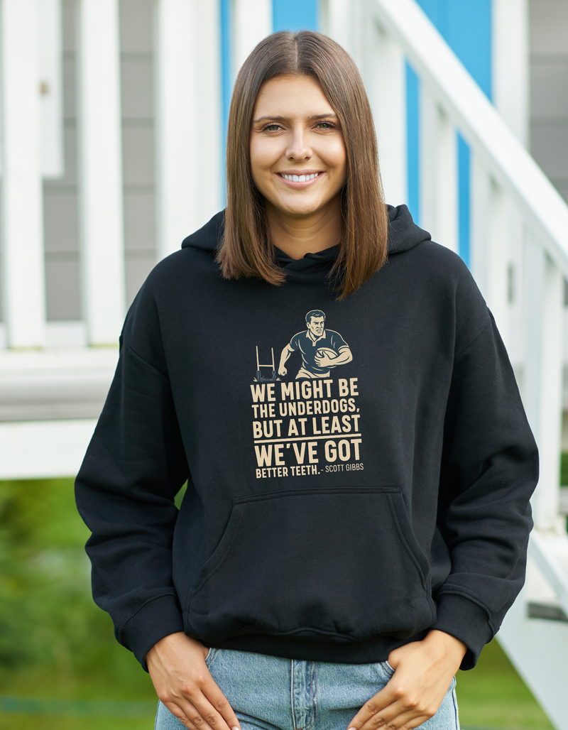 Person wearing a black hoodie with a graphic and text, standing outdoors, with slogan on the front saying 'We Might Be the Underdogs, but at Least We’ve Got Better Teeth – Scott Gibbs