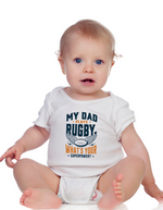 Baby wearing a white onesie with text about rugby and superpowers on a white background, with a slogan on the front saying 'My Dad Plays Rugby. What’s Your Superpower?