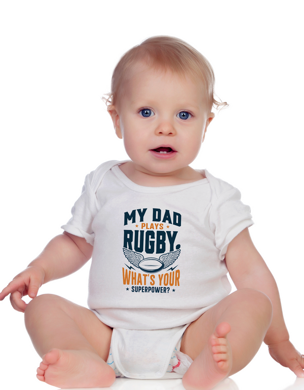 Baby wearing a white onesie with text about rugby and superpowers on a white background, with a slogan on the front saying 'My Dad Plays Rugby. What’s Your Superpower?