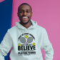 A man wearing a white hoodie with funny tennis slogan on the front that reads 'A white ceramic mug with tennis slogan on the front that reads 'I Wake Up Every Morning and Still Can’t Believe I Actually Make a Living Playing Tennis.'