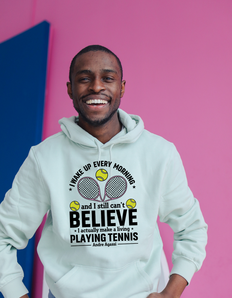 A man wearing a white hoodie with funny tennis slogan on the front that reads 'A white ceramic mug with tennis slogan on the front that reads 'I Wake Up Every Morning and Still Can’t Believe I Actually Make a Living Playing Tennis.'