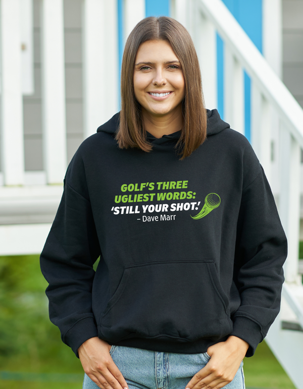 Person wearing a black hoodie with humorous text, standing outdoors with a Cows Corner slogan saying Golf, Three ugliest words, still your short - Dave Marr