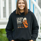 Woman wearing a black hoodie with a graphic design and text, standing outdoors, with slogan on the front saying 'I’ve Seen Better Hands on a Clock – Phil Kearns