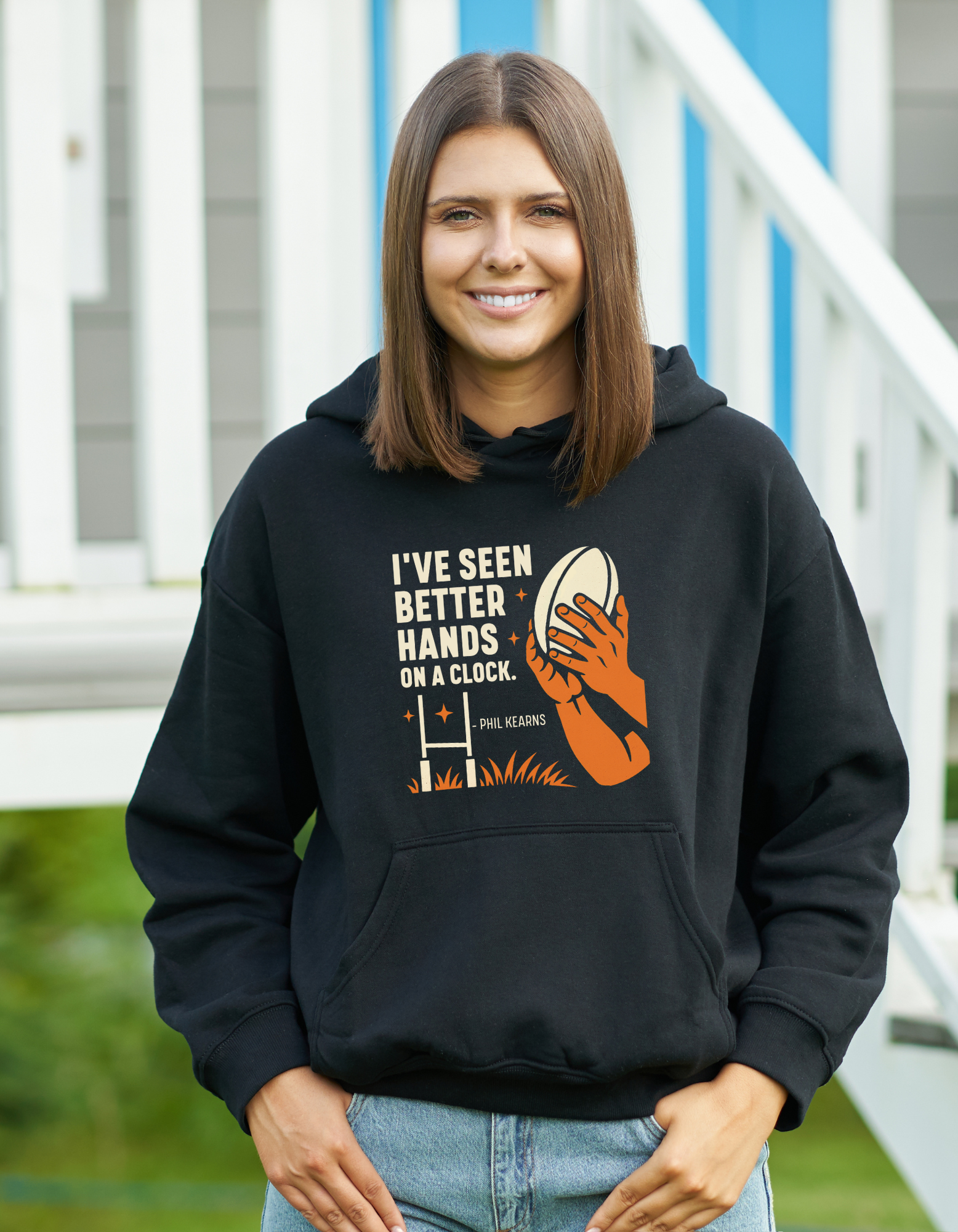 Woman wearing a black hoodie with a graphic design and text, standing outdoors, with slogan on the front saying 'I’ve Seen Better Hands on a Clock – Phil Kearns