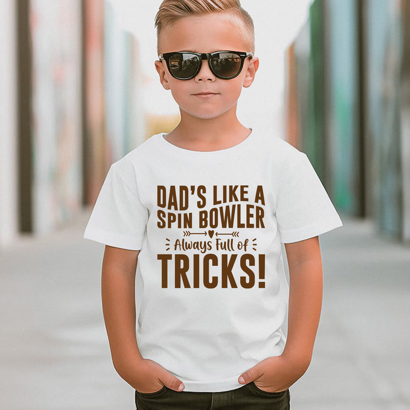 A little boy wearing a white t-shirt with Funny Cricket T-Shirt – "Dad’s Like a Spin Bowler, Always Full of Tricks!" on the front. A funny T-shirt, Premium Fabric, Multiple Junior Sizes, Perfect for Boys and Girls