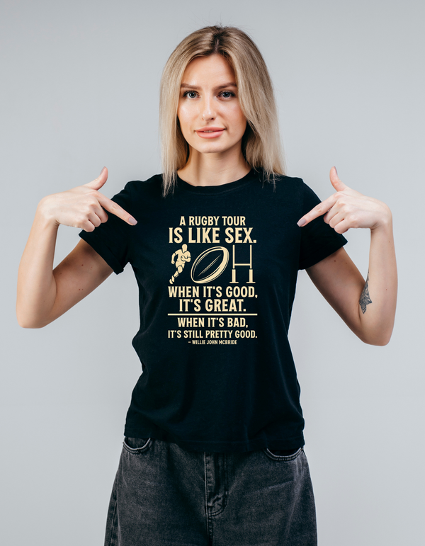Woman wearing a black t-shirt with humorous text design, pointing at the shirt, with the slogan on the front 'A Rugby Tour Is Like Sex. When It’s Good, It’s Great. When It’s Bad, It’s Still Pretty Good – Willie John McBride