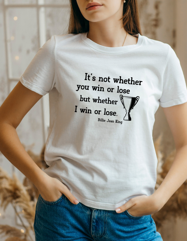 A lady wearing a white t-shirt with the funny tennis slogan on the front reading 'It’s Not Whether You Win or Lose but Whether I Win or Lose – Billie Jean-King!