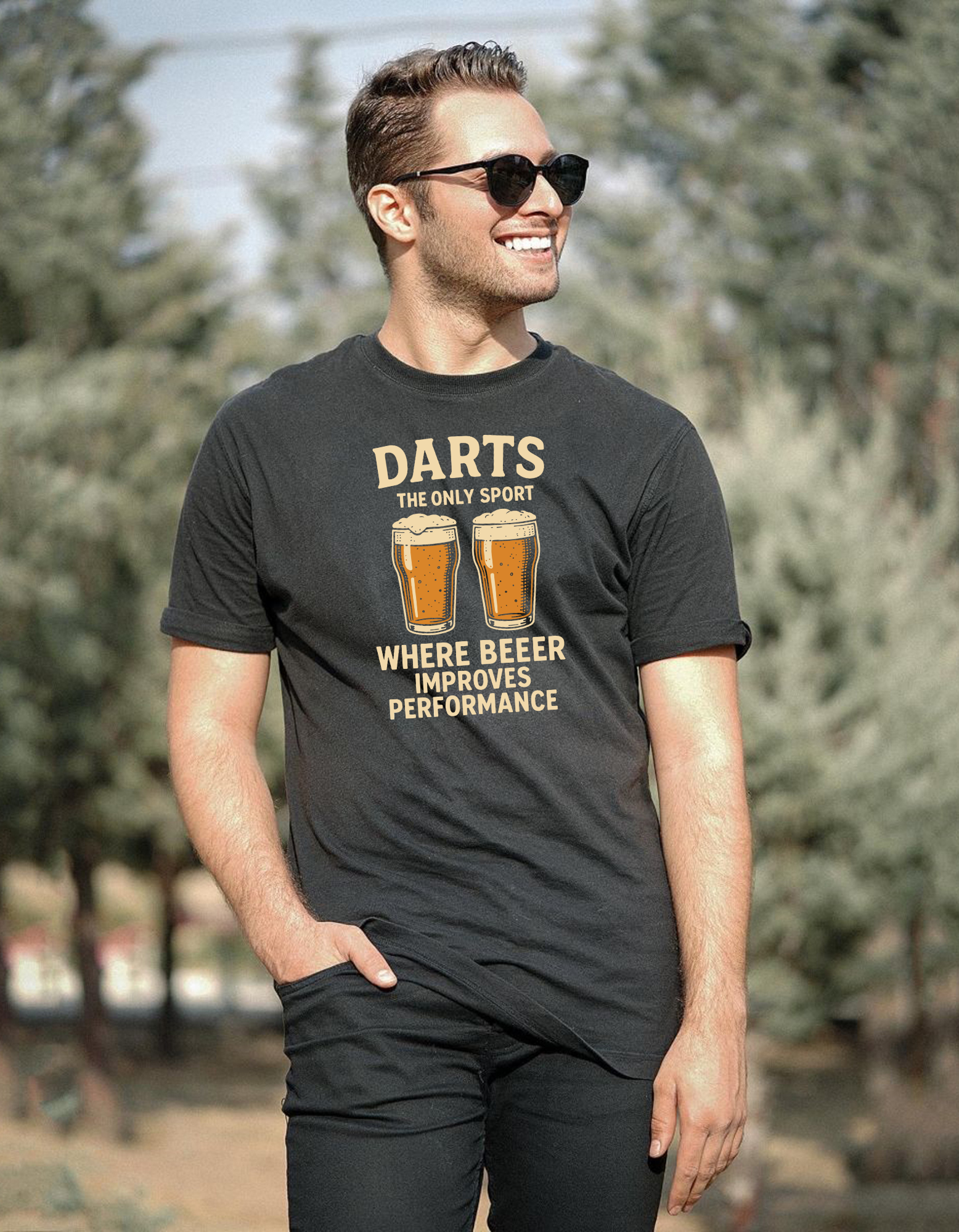 Man wearing a black t-shirt with a humorous dart and beer graphic, standing outdoors with a Cows Corner slogan saying Darts the only sport where beeer improves performance.
