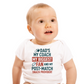 Baby wearing a white onesie with colorful text on a white background, with a slogan on the front saying 'Dad’s My Coach My Biggest Fan and My Post-Match Snack Provider!