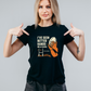 Woman wearing a black t-shirt with a graphic and text, pointing at the shirt, slogan saying 'I’ve Seen Better Hands on a Clock – Phil Kearns'