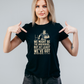 Woman wearing a black t-shirt with a graphic and text, pointing at the shirt, with slogan on the front saying 'We Might Be the Underdogs, but at Least We’ve Got Better Teeth – Scott Gibbs'
