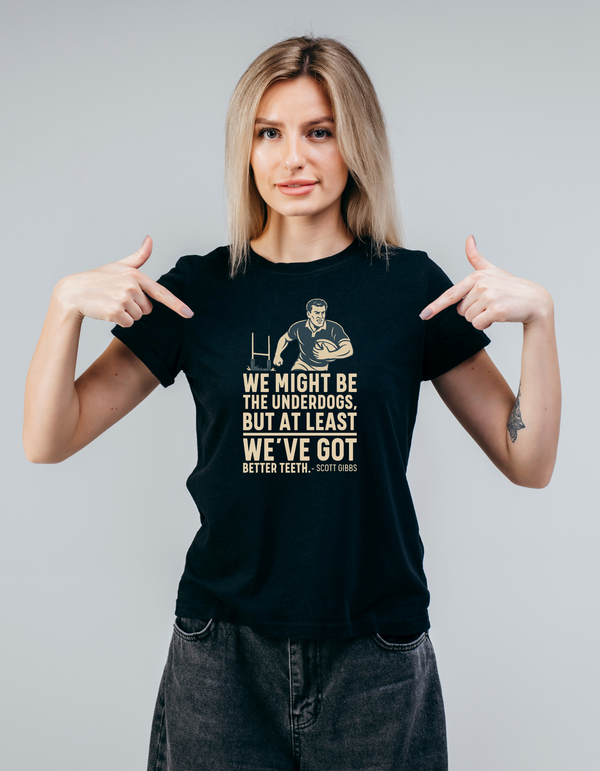 Woman wearing a black t-shirt with a graphic and text, pointing at the shirt, with slogan on the front saying 'We Might Be the Underdogs, but at Least We’ve Got Better Teeth – Scott Gibbs'