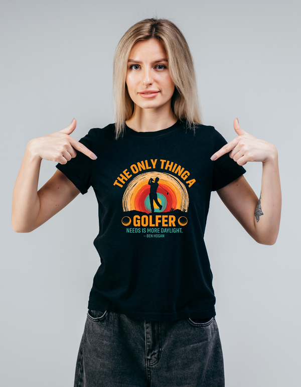 Woman wearing a black t-shirt with a colorful graphic and text, pointing at the shirt with a Cows Corner slogan saying The only thin a gold needs is more daylight - Ben Hogan