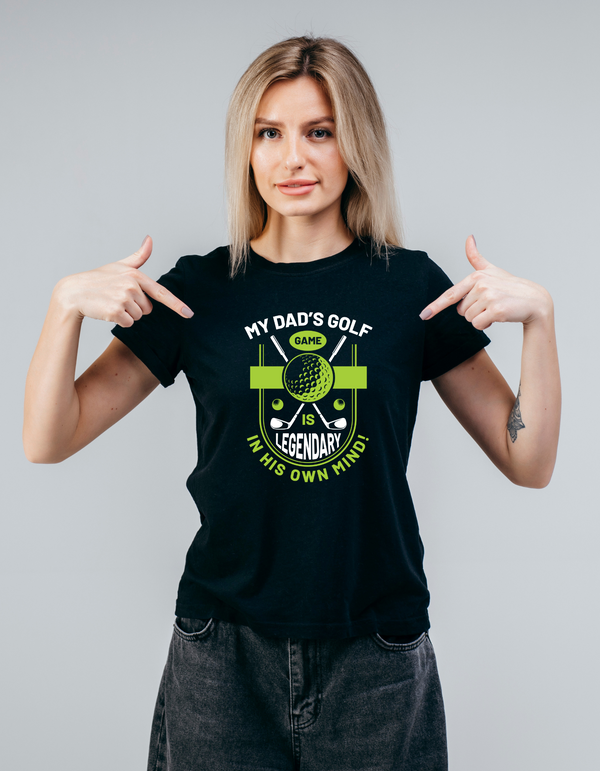Woman wearing a black t-shirt with a golf-themed graphic and text, pointing at the shirt with a Cows Corner slogan, my dad's golf game is legendary in his own mind.