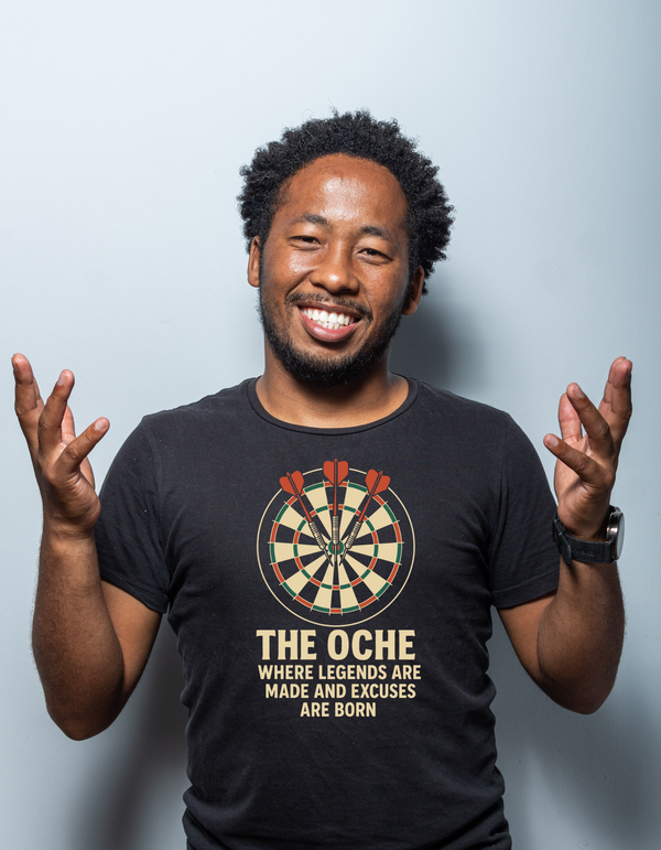 Man wearing a black t-shirt with a dartboard graphic and text, against a light gray background with a Cows Corner slogan The oche where legends are made and excuses are born.
