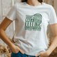 A lady wearing a white T-shirt with a funny tennis slogan on the front saying 'Winning Wimbledon Was a Great Feeling, but I Hadn’t Started Shaving Yet – Boris Becker'