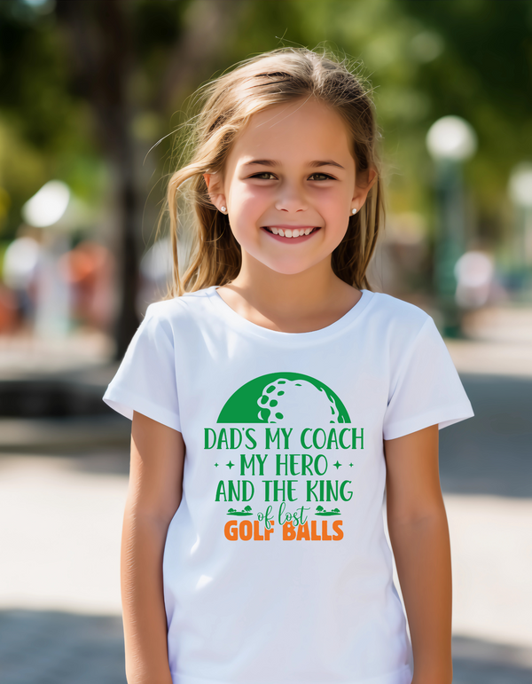 Young girl wearing a white t-shirt with a colorful graphic and text, standing outdoors with a Cows Corner slogan, Best dad by par.