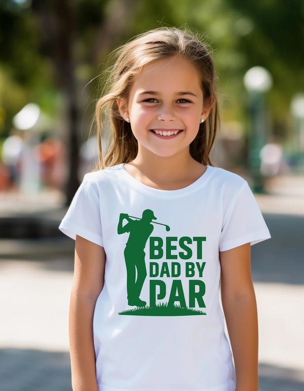 Young girl wearing a white t-shirt with a green graphic and text, standing outdoors with a Cows Corner slogan, Best dad by par.