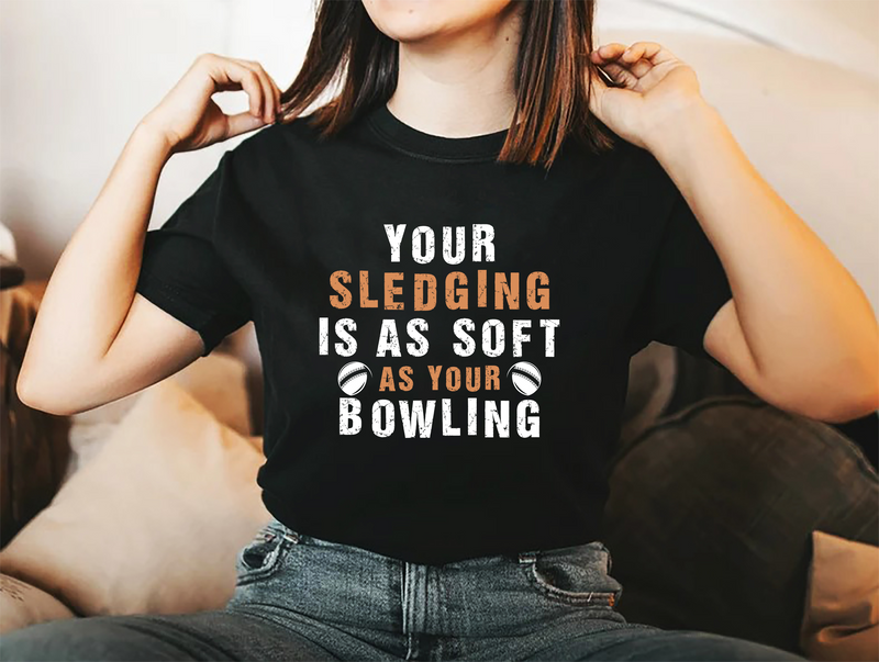 A lady wearing a black t-shirt with Your Sledging Is As Soft As Your Bowling on the front. A Funny Cricket T-Shirt, Premium Fabric, Multiple Adult Sizes
