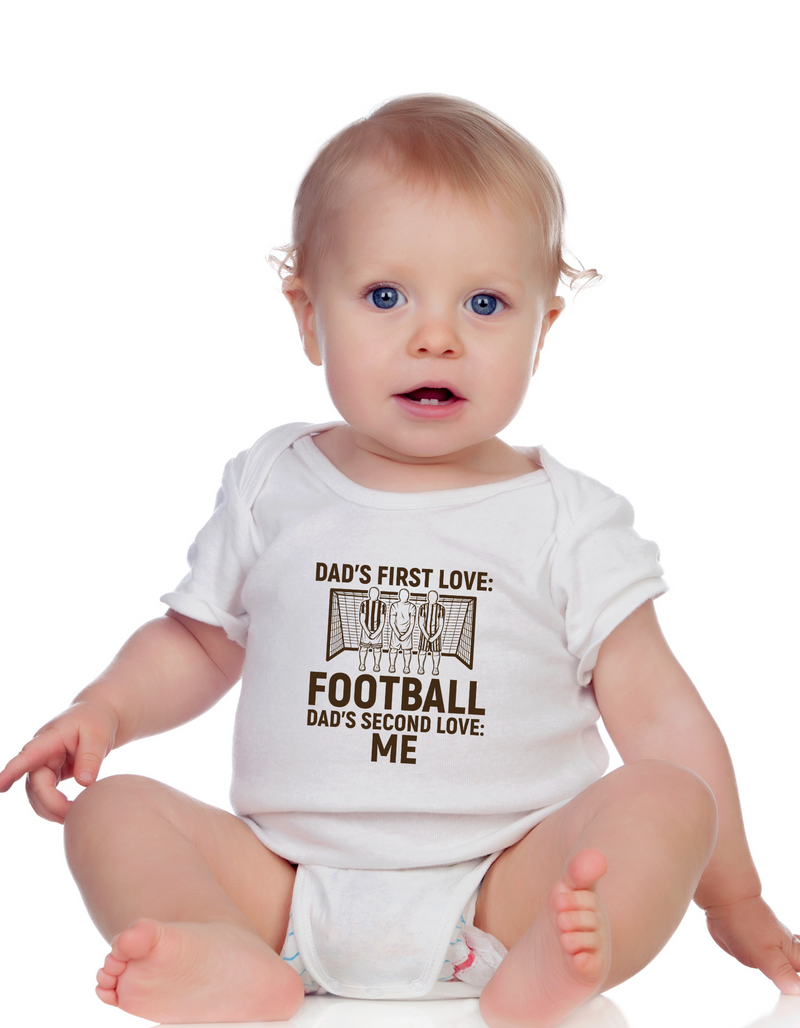 A baby wearing a white baby grow with the funny football slogan on the front saying 'Dad’s First Love: Football. Dad’s Second Love: Me'