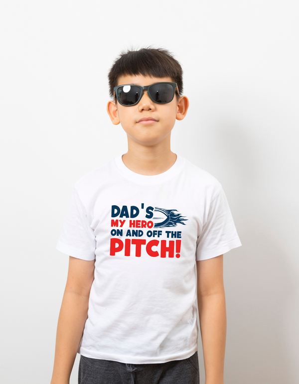 Child wearing a white t-shirt with a humorous message about a dad being a hero on and off the pitch with the Cows Corner slogan saying Dad's my hero on and off the pitch