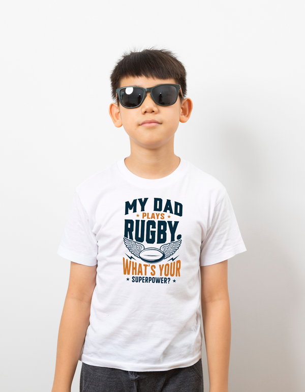 Child wearing a white t-shirt with rugby-themed text on a plain background, with a slogan on the front saying 'My Mum Tackles Everything on the Pitch and at Home!'