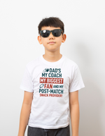 Child wearing a white t-shirt with humorous text design on a plain background, with a slogan on the front saying 'My Dad Plays Rugby. What’s Your Superpower?