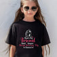 A little girl wearing a black t-shirt with Mum's My Personal Third Umpire, Always Reviewing My Choices on the front of the T-Shirt. Funny Cricket T-Shirt, Premium Fabric, Multiple Adult Sizes
