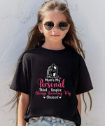 A little girl wearing a black t-shirt with Mum's My Personal Third Umpire, Always Reviewing My Choices on the front of the T-Shirt. Funny Cricket T-Shirt, Premium Fabric, Multiple Adult Sizes