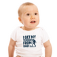 A little baby wearing a baby grow with the funny football slogan on the front saying 'I Get My Tekkers From Dad'