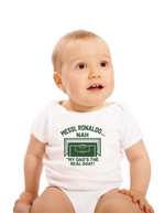A little baby wearing a white baby grow with the funny football and dad loving slogan on the front which reads 'Messi, Ronaldo…Nah ’My Dads the Real Goat!'