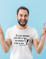 A man wearing a white t-shirt with the funny tennis slogan on the front reading 'It’s Not Whether You Win or Lose but Whether I Win or Lose – Billie Jean-King!