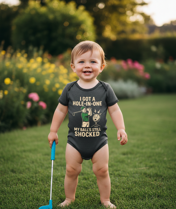 Child wearing a humorous onesie with a golfing design, standing outdoors in a garden. The baby is wearing a Cows Corner baby grow with a funny golf slogan 'I Got A Hole-In-One… My Ball’s Still Shocked'. Cows Corner gifts are perfect for sport-mad fans, these gifts work brilliantly for birthdays, new baby celebrations, Father’s Day, Mother’s Day, Christmas, anniversaries, thank you gifts, end-of-season team awards, graduations, retirements, and just-because moments when you want to raise a smile. 
