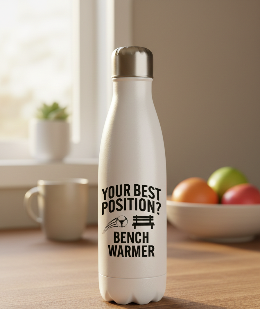 White water bottle with humorous text on a wooden surface with a bowl of fruit and mug in the background. This is a Cows Corner water bottle with a funny football slogan 'Your Best Position? Bench Warmer'. Cows Corner gifts are perfect for sport-mad fans, these gifts work brilliantly for birthdays, new baby celebrations, Father’s Day, Mother’s Day, Christmas, anniversaries, thank you gifts, end-of-season team awards, graduations, retirements, and just-because moments when you want to raise a smile. 
