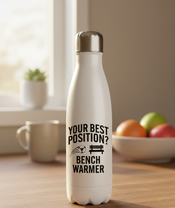 White water bottle with humorous text on a wooden surface with a bowl of fruit and mug in the background. This is a Cows Corner water bottle with a funny football slogan 'Your Best Position? Bench Warmer'. Cows Corner gifts are perfect for sport-mad fans, these gifts work brilliantly for birthdays, new baby celebrations, Father’s Day, Mother’s Day, Christmas, anniversaries, thank you gifts, end-of-season team awards, graduations, retirements, and just-because moments when you want to raise a smile. 
