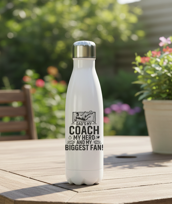 White water bottle with motivational quote on a wooden table outdoors. This is a Cows Corner water bottle with a funny football slogan 'Dad’s My Coach My Hero and My Biggest Fan!'. Cows Corner gifts are perfect for sport-mad fans, these gifts work brilliantly for birthdays, new baby celebrations, Father’s Day, Mother’s Day, Christmas, anniversaries, thank you gifts, end-of-season team awards, graduations, retirements, and just-because moments when you want to raise a smile. 
