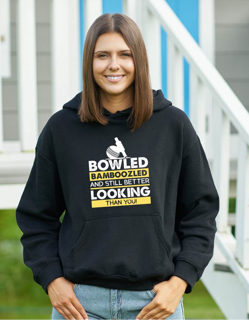 A lady wearing a black hoodie with Bowled & Bamboozled And Still Looking Better Than You on the front, A Funny Hoodie.  Funny Cricket Hoodie, Premium Fabric, Multiple Adult Sizes