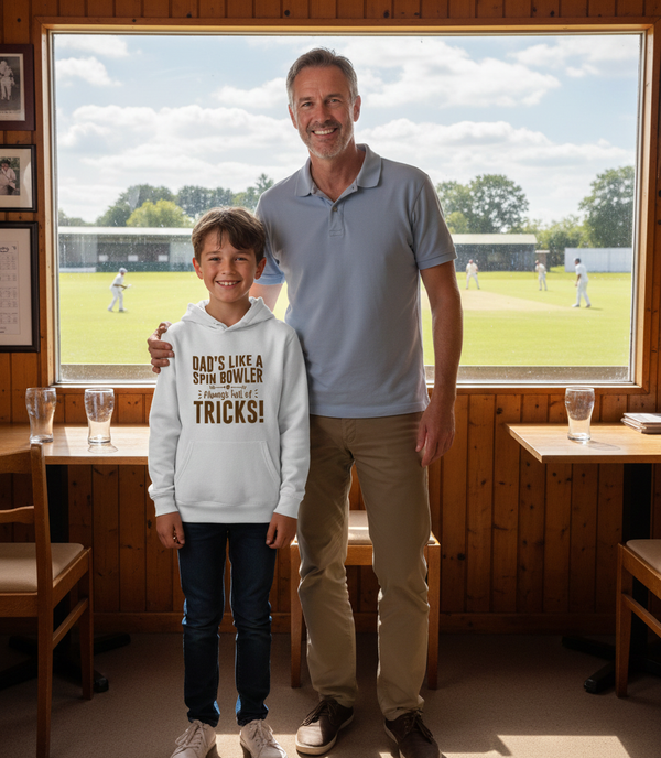 Man and child standing in a room with a view of a sports field outside a large window. The boy is wearing a Cows Corner hoodie with the funny cricket slogan 'Dad’s Like a Spin Bowler, Always Full of Tricks!'. Cows Corner gifts are perfect for sport-mad fans, these gifts work brilliantly for birthdays, new baby celebrations, Father’s Day, Mother’s Day, Christmas, anniversaries, thank you gifts, end-of-season team awards, graduations, retirements, and just-because moments when you want to raise a smile. 
