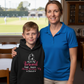 Woman and child standing together with a black hoodie with text, in front of a window showing a sports field. The boy is wearing a Cows Corner hoodie with the funny cricket slogan that reads 'Mum's My Personal Third Umpire, Always Reviewing My Choices'. Cows Corner gifts are perfect for sport-mad fans, these gifts work brilliantly for birthdays, new baby celebrations, Father’s Day, Mother’s Day, Christmas, anniversaries, thank you gifts, end-of-season team awards, graduations, retirements, and just-because 