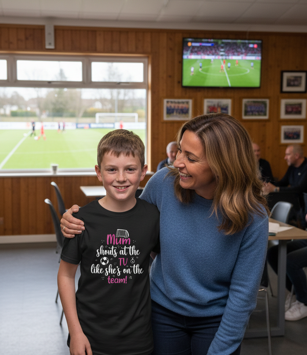 Woman and child in a sports facility with a TV screen showing a soccer match.  The boy is wearing a Cows Corner T-shirt with the funny and sweet slogan on the front that reads 'Mum Shouts at the TV Like She’s on the Team!'  Cows Corner gifts are perfect for sport-mad fans, these gifts work brilliantly for birthdays, new baby celebrations, Father’s Day, Mother’s Day, Christmas, anniversaries, thank you gifts, end-of-season team awards, graduations, retirements, and just-because moments 