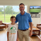 Man and young boy standing in a living room with a TV showing golf on the wall. The boy is wearing a Cows Corner t-shirt that has a funny and sweet golf saying on the front that reads 'Dads My Coach, My Hero and the King of Lost Golf Balls'. Cows Corner gifts are perfect for sport-mad fans, these gifts work brilliantly for birthdays, new baby celebrations, Father’s Day, Mother’s Day, Christmas, anniversaries, thank you gifts, end-of-season team awards, graduations, retirements, and just-because moments