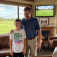 Man and young boy standing together in a living room with a TV showing a golf game. The boy is wearing a Cows Corner t-shirt with a funny and sweet golf saying on the front that reads 'Drive Chip Putt Hug Dad Repeat!'. Cows Corner gifts are perfect for sport-mad fans, these gifts work brilliantly for birthdays, new baby celebrations, Father’s Day, Mother’s Day, Christmas, anniversaries, thank you gifts, end-of-season team awards, graduations, retirements, and just-because moments