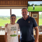 Two men standing together with a TV screen showing a golf game in the background. The boy is wearing a Cows Corner t-shirt with the golf coach slogan on the front that reads 'Thanks for Helping Me for the Fairway – and My Confidence'. Cows Corner gifts are perfect for sport-mad fans, these gifts work brilliantly for birthdays, new baby celebrations, Father’s Day, Mother’s Day, Christmas, anniversaries, thank you gifts, end-of-season team awards, graduations, retirements, and just-because moments 