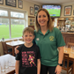 Woman and child standing together in a sports bar with a TV showing a game. The boy is wearing a Cows Corner t-shirt with a funny and sweet rugby slogan that reads 'Mum Rucks, Mum Tackles, Mum Wins at Life!'. Cows Corner gifts are perfect for sport-mad fans, these gifts work brilliantly for birthdays, new baby celebrations, Father’s Day, Mother’s Day, Christmas, anniversaries, thank you gifts, end-of-season team awards, graduations, retirements, and just-because moments when you want to raise a smile. 
