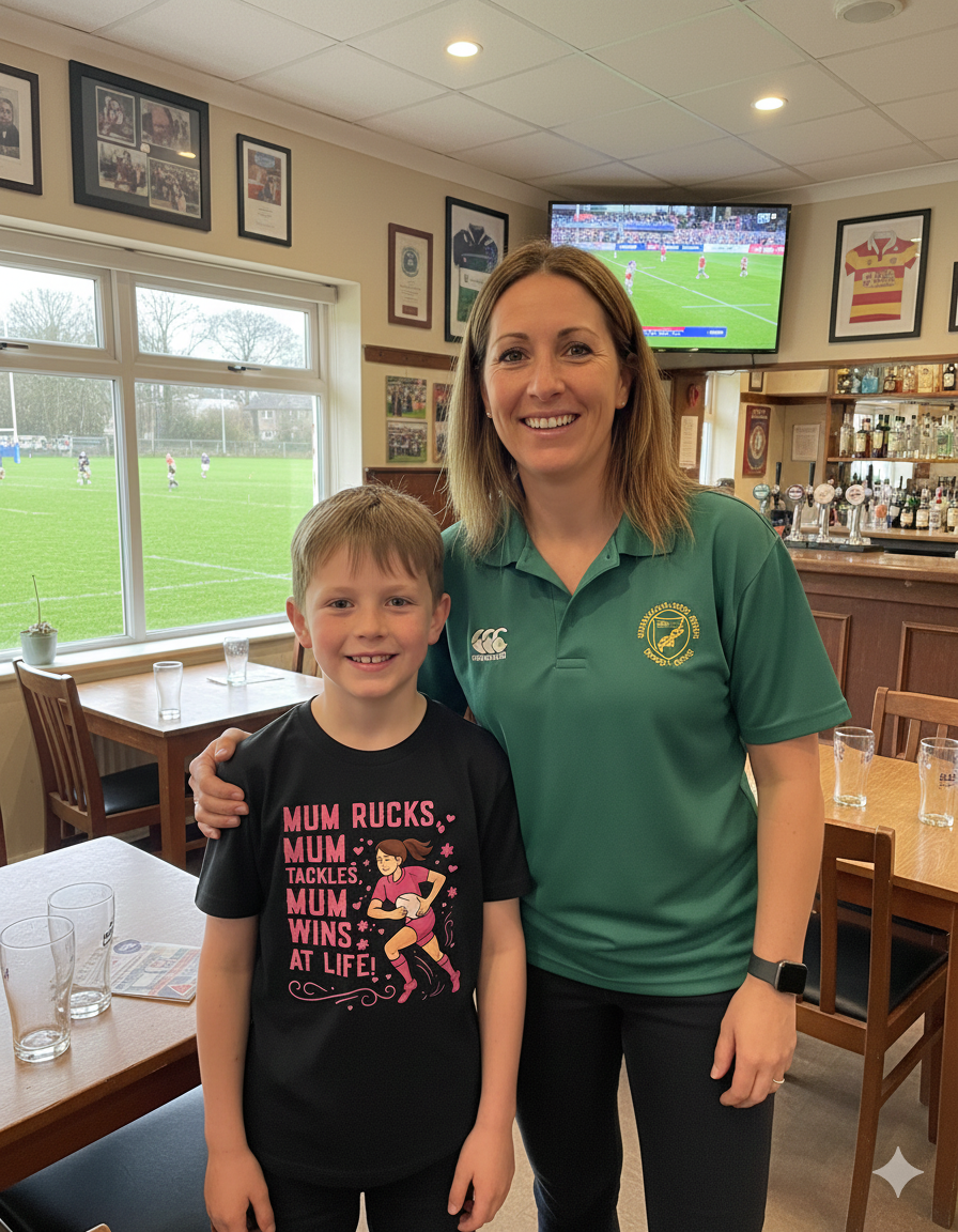 Woman and child standing together in a sports bar with a TV showing a game. The boy is wearing a Cows Corner t-shirt with a funny and sweet rugby slogan that reads 'Mum Rucks, Mum Tackles, Mum Wins at Life!'. Cows Corner gifts are perfect for sport-mad fans, these gifts work brilliantly for birthdays, new baby celebrations, Father’s Day, Mother’s Day, Christmas, anniversaries, thank you gifts, end-of-season team awards, graduations, retirements, and just-because moments when you want to raise a smile. 
