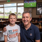 Man and young boy sitting together in a sports bar with a TV showing a rugby match. The boy is wearing a Cows Corner t-shirt with the funny and sweet rugby slogan on the front that reads 'My Dad Tackles Life Like a Rugby Match- Head First'. Cows Corner gifts are perfect for sport-mad fans, these gifts work brilliantly for birthdays, new baby celebrations, Father’s Day, Mother’s Day, Christmas, anniversaries, thank you gifts, end-of-season team awards, graduations, retirements, and just-because moments 