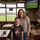Woman and child in a pub with a television showing a rugby match. The boy is wearing a Cows Corner t-shirt with the funny and sweet rugby slogan 'Mum Rucks, Mum Tackles, Mum Wins at Life!'. Cows Corner gifts are perfect for sport-mad fans, these gifts work brilliantly for birthdays, new baby celebrations, Father’s Day, Mother’s Day, Christmas, anniversaries, thank you gifts, end-of-season team awards, graduations, retirements, and just-because moments when you want to raise a smile. 
